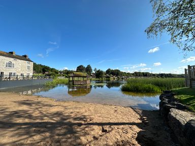 A lakeside view with a stone building and a wooden gazebo on the water at Lakeside 18 in Carnforth