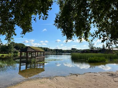 A lake with a wooden gazebo on the water and houses in the background at Lakeside 18 in Carnforth