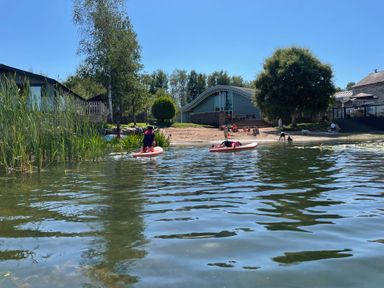 A lake scene with people paddleboarding near the shore and a sandy beach with several people and buildings in the background at Lakeside 18 in Carnforth