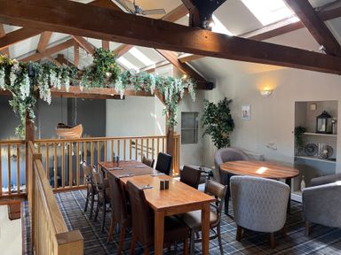 A dining area with wooden tables and chairs and decorative greenery on beams at Lakeside 18 in Carnforth