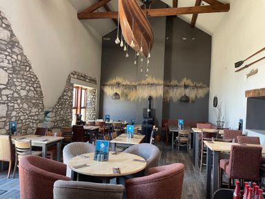 A dining area with multiple wooden tables and chairs under a high ceiling with exposed wooden beams and a boat-shaped light fixture at Lakeside 18 in Carnforth