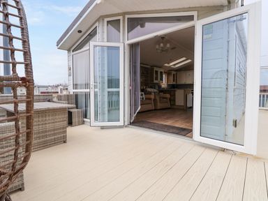 An outdoor patio with wicker furniture and a hanging chair next to an open door leading to a living area at Hazel Park Lodge HP4 in Rhyl
