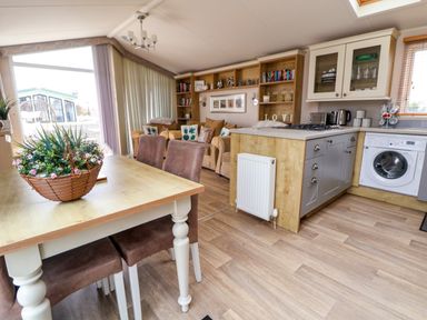 An open living room and kitchen area with a dining table with a flower basket on it at Hazel Park Lodge HP4 Rhyl