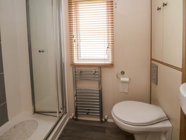 A bathroom with a toilet a shower a window with blinds and a towel radiator at Hazel Park Lodge HP4 in Rhyl
