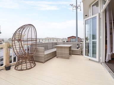 An outdoor deck area with wicker seating and a table next to an open patio door at Hazel Park Lodge HP4 in Rhyl