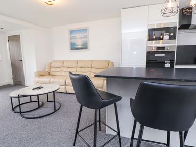 A living room with a sofa, coffee table, and kitchen area at 4 Willow Grove - Freehold Talacre