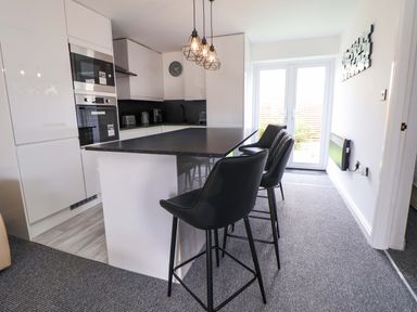 A kitchen with a counter and stools at 4 Willow Grove - Freehold Talacre
