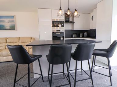 A kitchen with bar stools and appliances at 4 Willow Grove - Freehold in Talacre