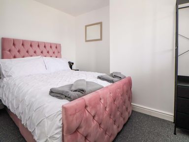 A bedroom with a pink bed and white linens at 4 Willow Grove - Freehold Talacre