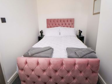 A bedroom with a pink bed and towels on the bed at 4 Willow Grove - Freehold Talacre