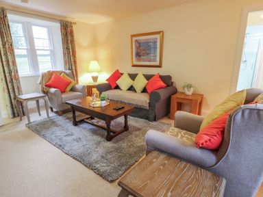 A living room with sofas a coffee table a lamp and windows at Eagle Glen Cottage in Kettins near Coupar Angus
