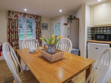 A dining table with white chairs a vase with yellow flowers a teapot and a cup in a cottage kitchen at Eagle Glen Cottage in Kettins near Coupar Angus