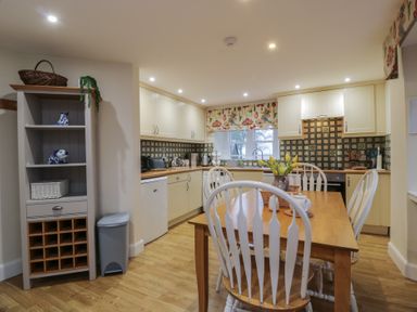 A kitchen with a wooden dining table and white chairs and a shelving unit with ceramics at Eagle Glen Cottage Kettins near Coupar Angus