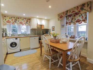 A kitchen with wooden table and four chairs near floral curtains on windows at Eagle Glen Cottage in Kettins near Coupar Angus
