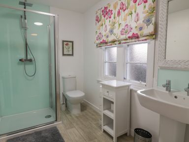 A bathroom with shower, toilet, sink, storage cabinet and floral window blinds at Eagle Glen Cottage in Kettins near Coupar Angus
