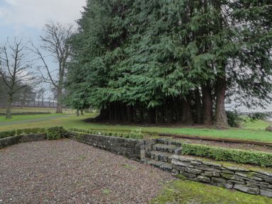 A garden area with stone steps and walls next to a group of large evergreen trees at Eagle Glen Cottage Kettins near Coupar Angus