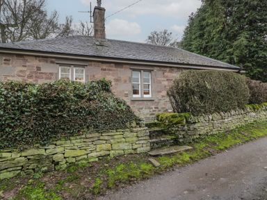 A stone cottage with two windows behind a stone wall and trimmed hedges at Eagle Glen Cottage Kettins near Coupar Angus