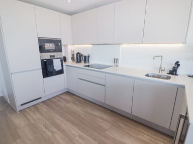 A kitchen with white cabinets built-in appliances a sink and wooden floor at The Links 40 An apartment with spectacular sea views in Porthcawl