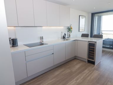 A kitchen with white cabinets a stovetop a sink a wine cooler and bar stools at The Links 40 An apartment with spectacular sea views Porthcawl