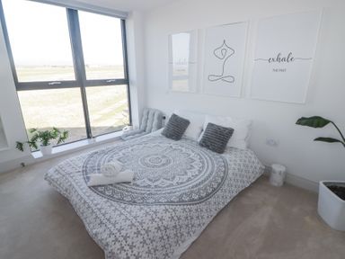 A bedroom with a bed pillows wall art plants and large window at The Links 40 in Porthcawl