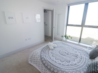 A bedroom with a patterned bedspread a closet three framed pictures and a large window at The Links 40 An apartment with spectacular sea views in Porthcawl