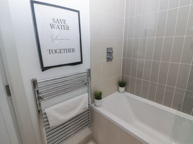 A bathroom with a bathtub two small potted plants a towel rack with a towel and a framed sign at The Links 40 an apartment with spectacular sea views in Porthcawl