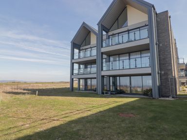 A modern multi-story building with balconies and large windows on a grassy area at The Links 40 An apartment with spectacular sea views Porthcawl