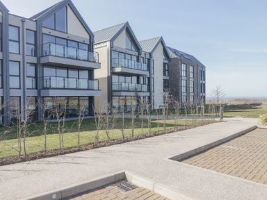 Modern apartment buildings with glass balconies and a paved pathway at The Links 40 An apartment with spectacular sea views in Porthcawl