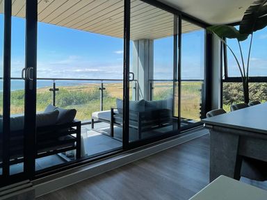 A balcony with outdoor seating overlooking a landscape seen through glass doors at The Links 40 in Porthcawl