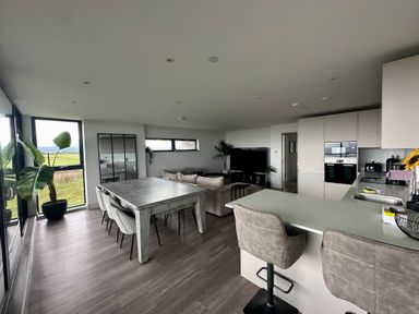 An open plan kitchen and living room with a dining table chairs sofas and large windows at The Links 40 An apartment with spectacular sea views in Porthcawl