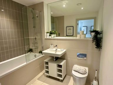 A bathroom with a bathtub shower and a sink with storage and a toilet with a roll on top at The Links 40 An apartment with spectacular sea views Porthcawl