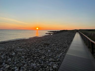 A pebble beach at sunset with a wooden boardwalk alongside at The Links 40 An apartment with spectacular sea views in Porthcawl