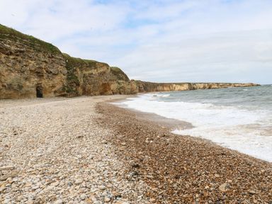 A pebble beach with cliffs on the left and waves from the sea on the right at The Beach Apartment in South Shields