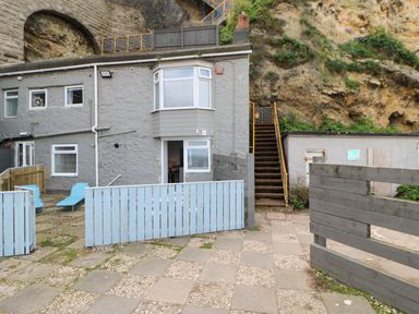 An outdoor patio area with two blue lounge chairs a stone building with windows and a door and a set of stairs leading up a rocky hillside at The Beach Apartment in South Shields