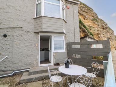 An outdoor patio with a round table and four chairs with a bottle in an ice bucket on the table outside a grey stone building at The Beach Apartment in South Shields