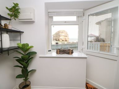 A corner of a room with a potted plant a black metal wall shelf and a window with a view of a large rock by the sea at The Beach Apartment in South Shields