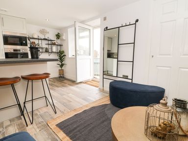 An open kitchen and living area with bar stools plant open door and oval ottoman at The Beach Apartment in South Shields