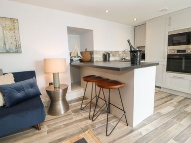 A kitchen with a black countertop island two brown stools a silver lamp and a blue sofa at The Beach Apartment in South Shields
