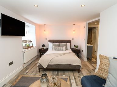 A bedroom with a bed two bedside tables hanging lights a wall-mounted tv and a small seating area at The Beach Apartment in South Shields