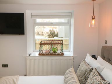 A bedroom with a window, a mounted TV, a radiator, and a bed with patterned pillows at The Beach Apartment in South Shields