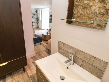 A bathroom sink with a faucet and mirror above and a view into a living area with furniture and an open door at The Beach Apartment in South Shields