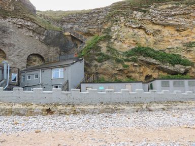 A stone wall and buildings at the base of a rocky cliff with stairs leading up at The Beach Apartment in South Shields