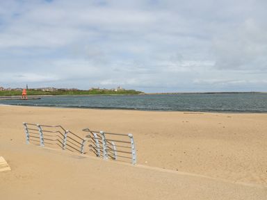 A sandy beach with metal railings and a body of water at The Beach Apartment in South Shields