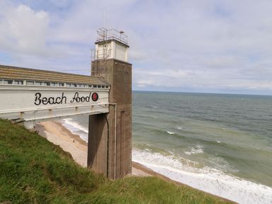 A coastal structure with a tower and a sign reading beach food overlooking a beach and ocean at The Beach Apartment in South Shields