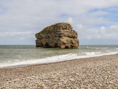 A rocky sea stack in the ocean near a pebble beach at The Beach Apartment in South Shields