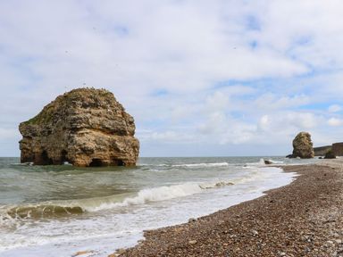 A pebble beach with two large rock formations in the sea under a cloudy sky at The Beach Apartment in South Shields
