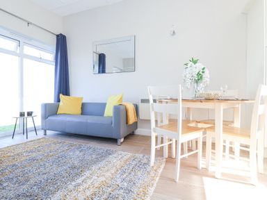 A living room with a gray sofa yellow pillows a wooden dining table with white chairs and flowers on it at Atlantic Escape in Widemouth Bay