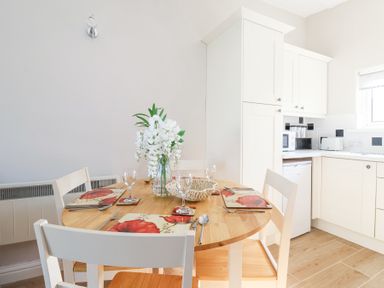 A dining table set for four with white flowers in a vase in a kitchen at Atlantic Escape in Widemouth Bay