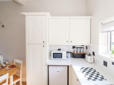 A kitchen countertop with a microwave, toaster, canisters and a small fridge under the counter at Atlantic Escape in Widemouth Bay