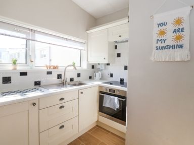A kitchen with white cabinets a stainless steel sink stove and oven a kettle and a decorative wall hanging Atlantic Escape Widemouth Bay